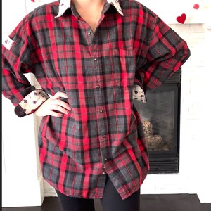 May include: Red and black plaid button-down shirt with a contrasting patterned collar and cuffs. The shirt has a classic lumberjack style with a pocket on the chest. The cuffs and collar feature a cream-colored fabric with a small geometric pattern.