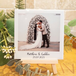 May include: A white ceramic tile with a wedding photograph of a couple kissing, set against a floral backdrop. The tile is displayed on a small wooden easel. The names "Matthew & Gabbie" and the date "23.07.2023" are printed on the tile.