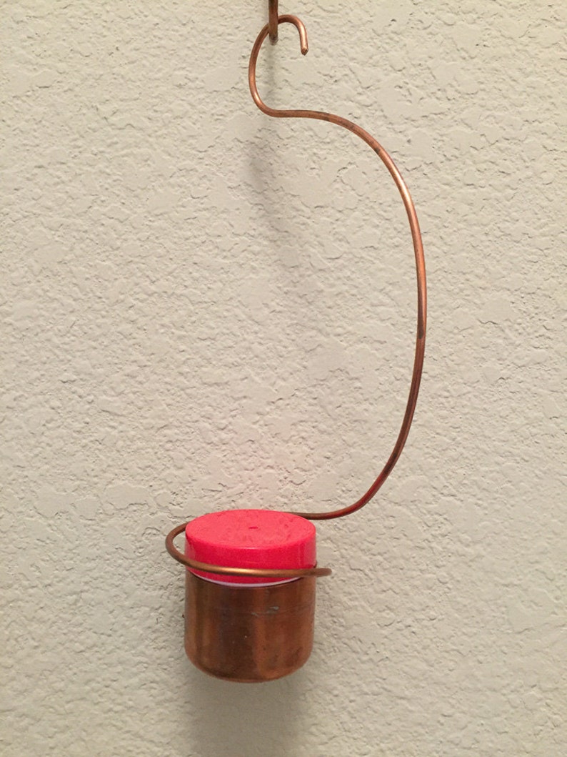 May include: A copper hummingbird feeder with a red plastic top hanging from a copper wire hook.