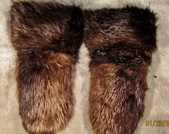 May include: A pair of brown fur mittens with a cuff. The mittens are made of a soft, fluffy fur.