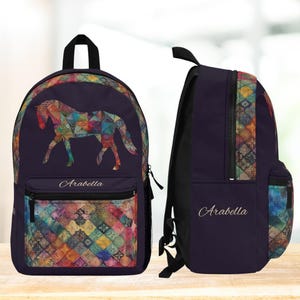 May include: A purple backpack with a colorful horse design and the name "Arabella" embroidered on the front. The backpack has a zippered pocket on the front and a side pocket.