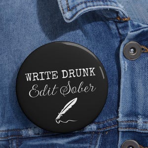 May include: A black button with white text that reads "Write Drunk Edit Sober" and a white illustration of a quill pen.