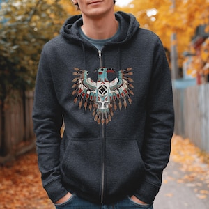 May include: Dark gray zip-up hoodie featuring a detailed Native American-inspired eagle design on the front. The eagle has a turquoise head, red beak, and intricate feather details in shades of brown, red, and white. The hoodie has a drawstring hood and a full-length zipper.