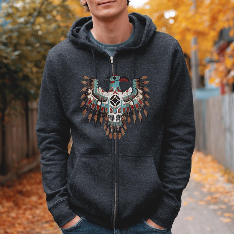 May include: Dark gray zip-up hoodie featuring a detailed Native American-inspired eagle design on the front. The eagle has a turquoise head, red beak, and intricate feather details in shades of brown, red, and white. The hoodie has a drawstring hood and a full-length zipper.