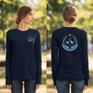 Könnte beinhalten: Marineblaues Langarmshirt mit einem kreisförmigen Logo auf Vorder- und Rückseite. Das vordere Logo hat blaue und weiße Akzente. Auf der Rückseite befindet sich ein Vogel- und Sternmotiv in einem gepunkteten Kreis.