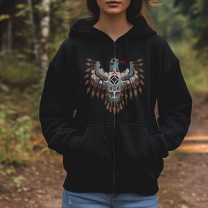May include: Black zip-up hoodie featuring a detailed Native American-inspired design on the front. The design includes a stylized eagle with blue, red, and brown accents, and a geometric center. The hoodie has a drawstring hood and two front pockets.