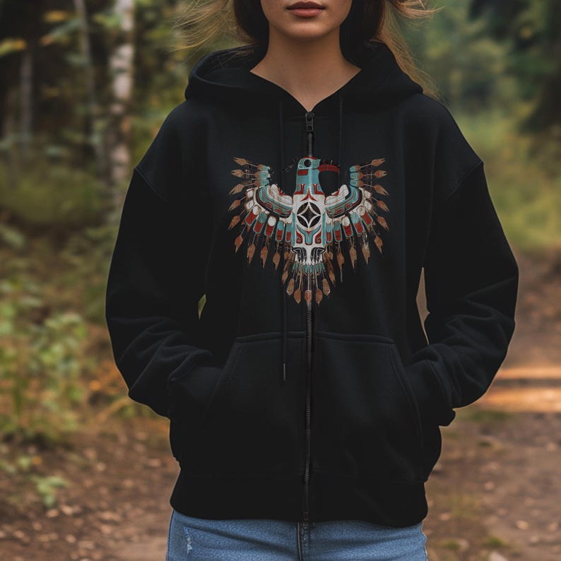 May include: Black zip-up hoodie featuring a detailed Native American-inspired design on the front. The design includes a stylized eagle with blue, red, and brown accents, and a geometric center. The hoodie has a drawstring hood and two front pockets.