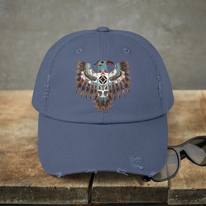 Puede incluir: Una gorra de béisbol azul desgastada con un diseño de águila nativo americana colorido. El águila está representada en un estilo tradicional con detalles intrincados y colores vibrantes.