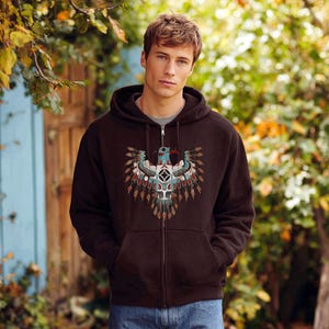 May include: A dark brown zip-up hoodie featuring a detailed Native American-inspired design on the front. The design includes a stylized eagle with teal, red, and white accents. The hoodie has a hood and front pockets, perfect for casual wear.