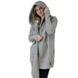 May include: A gray hooded cardigan with a long, asymmetrical hemline. The cardigan has a zipper closure and two pockets. The model is wearing black pants and black boots.