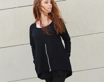 May include: A woman wearing a black long-sleeved shirt with a zipper and black pants. She is wearing black and white sneakers.