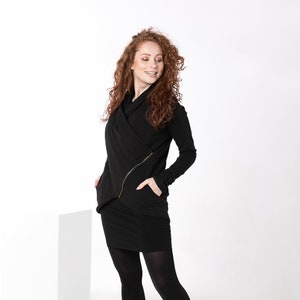 May include: A woman wearing a black long-sleeved wrap dress with a zipper detail and black tights. She is wearing black lace-up boots and has long, curly red hair.