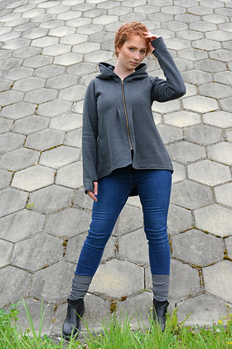 Pode incluir: Uma jaqueta de moletom cinza com capuz e fecho de z&iacute;per. A modelo est&aacute; usando jeans azul e meias cinzas com botas pretas.