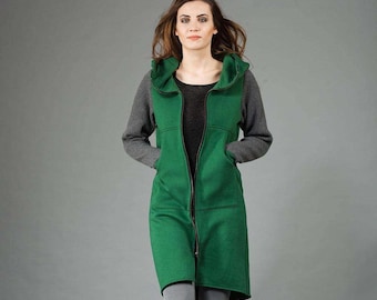 May include: A long, green hooded vest with a full-length zipper. The vest has a tailored fit and is paired with gray knit sleeves and a dark gray top. The model is wearing gray pants. The vest has two front pockets.