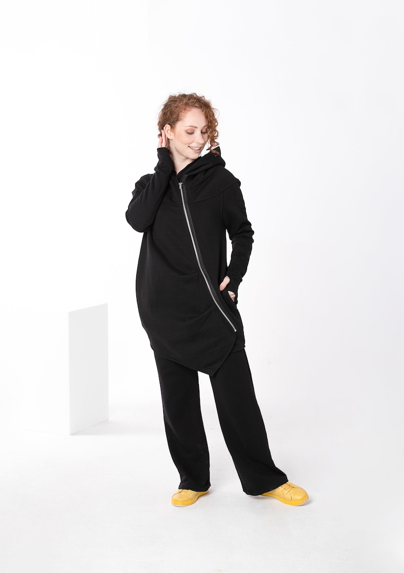 May include: A black hooded sweatshirt with a long, asymmetrical hem and a zipper down the front. The sweatshirt has thumbholes at the cuffs.
