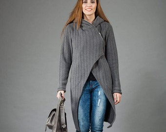 May include: A woman wearing a gray hooded sweater with a zipper and a long, asymmetrical hem. She is carrying a gray leather bag and wearing blue jeans.