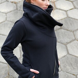 May include: A black zippered jacket with a large, folded collar. The jacket has a long sleeve and a zipper on the front. The jacket is made of a soft, comfortable material.