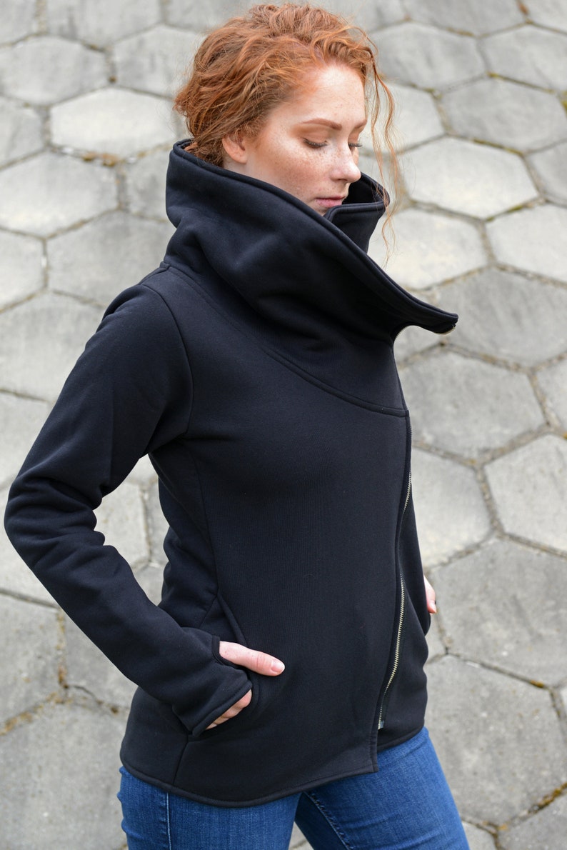 May include: A black zippered jacket with a large, folded collar. The jacket has a long sleeve and a zipper on the front. The jacket is made of a soft, comfortable material.