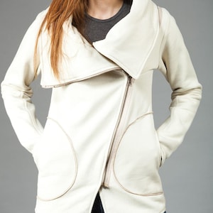 May include: A white zippered jacket with a large, folded collar. The jacket has two large pockets on the front and a zipper closure.