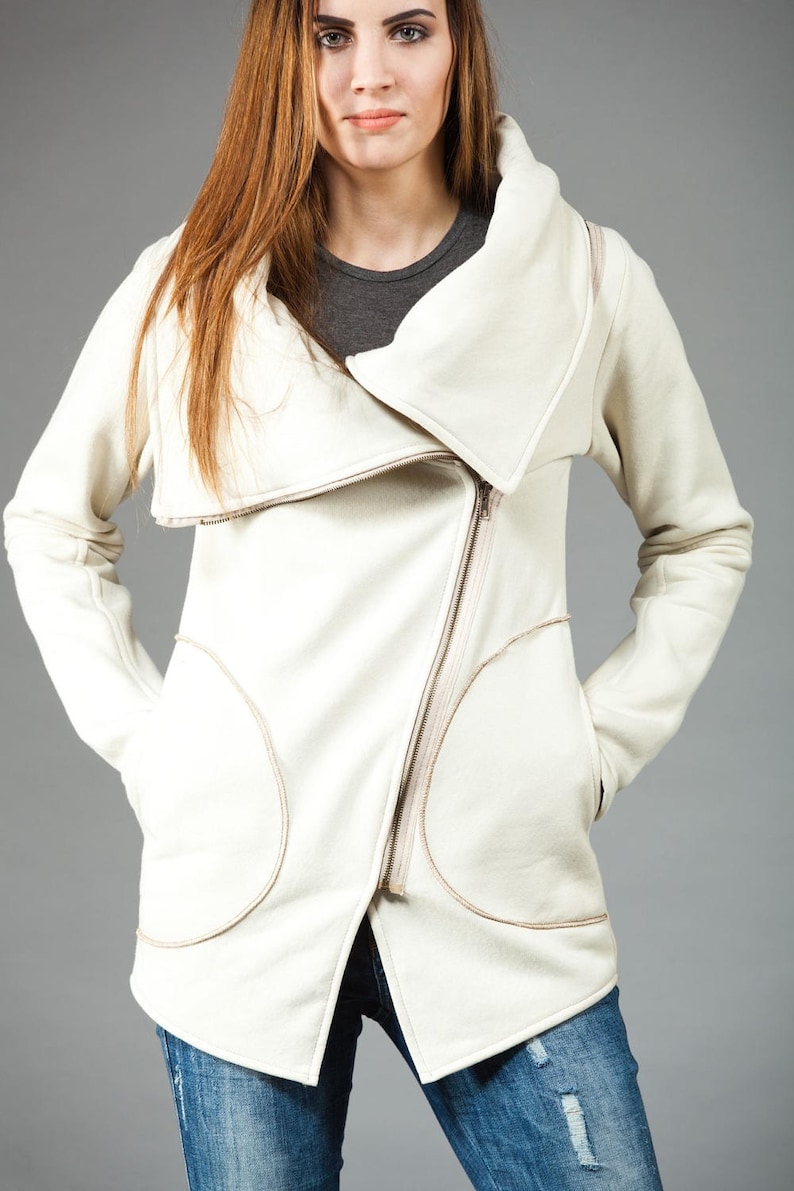 May include: A white zippered jacket with a large, folded collar. The jacket has two large pockets on the front and a zipper closure.