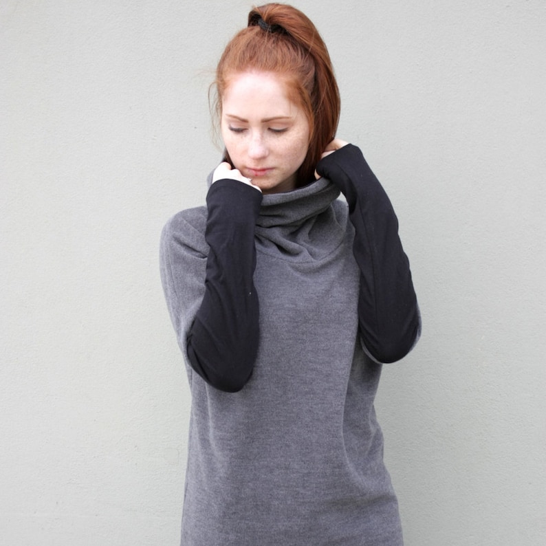 K&ouml;nnte beinhalten: Ein grauer Rollkragenpullover mit schwarzen &Auml;rmeln. Der Pullover hat eine lockere Passform und einen hohen Kragen.