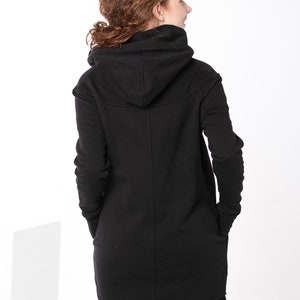 May include: A black hooded sweatshirt with a long, asymmetrical hemline. The sweatshirt has a relaxed fit and a drawstring hood.