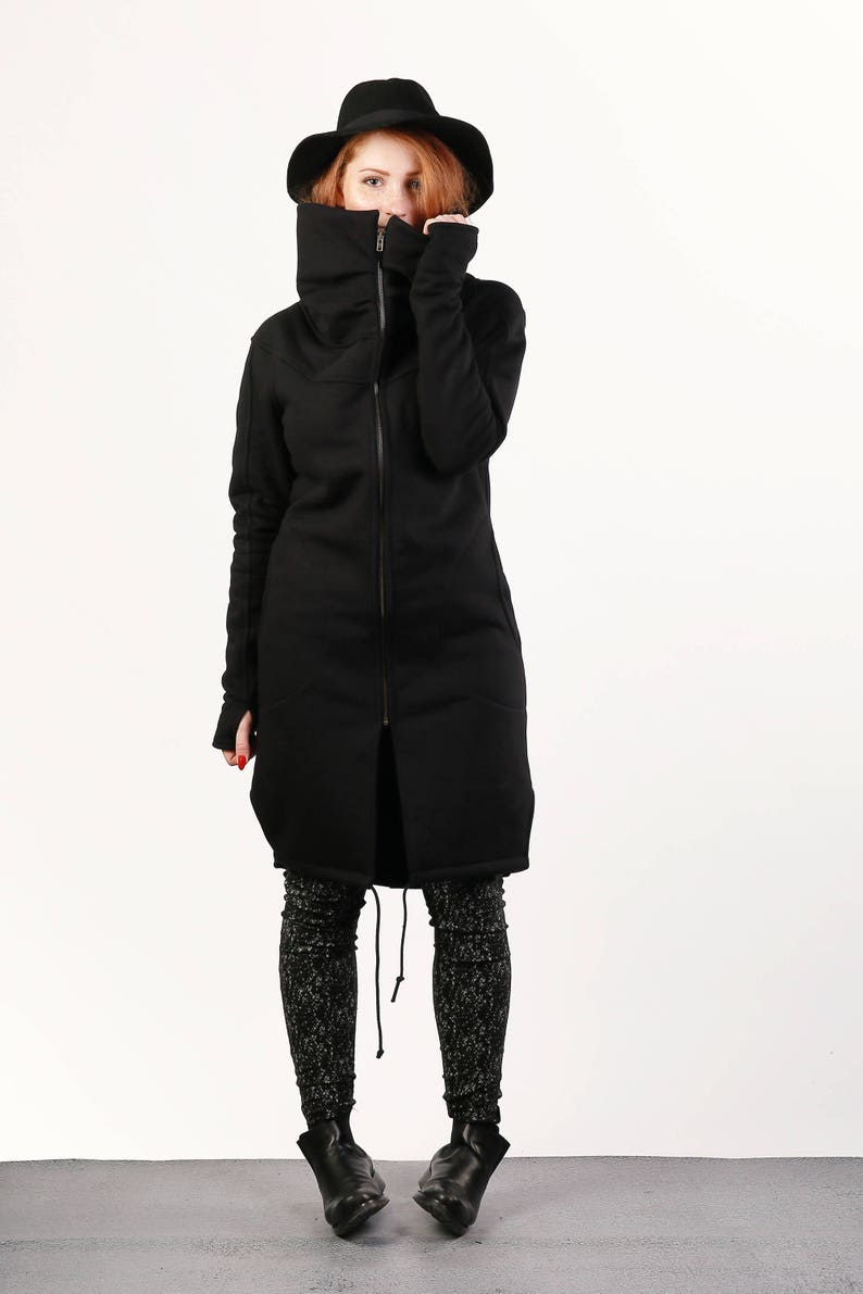 May include: A black long-sleeved jacket with a high collar and a zipper closure. The jacket has a relaxed fit and a slightly longer length. The model is wearing the jacket with black leggings and black boots.