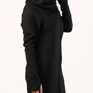May include: A black long-sleeved jacket with a high collar and a zipper closure. The jacket has a relaxed fit and a slightly oversized look. The model is wearing a black hat and black pants.