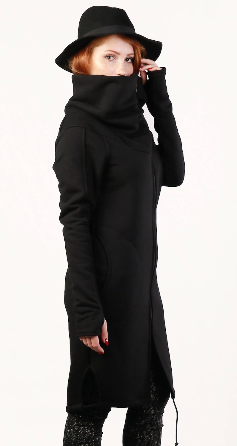 May include: A black long-sleeved jacket with a high collar and a zipper closure. The jacket has a relaxed fit and a slightly oversized look. The model is wearing a black hat and black pants.