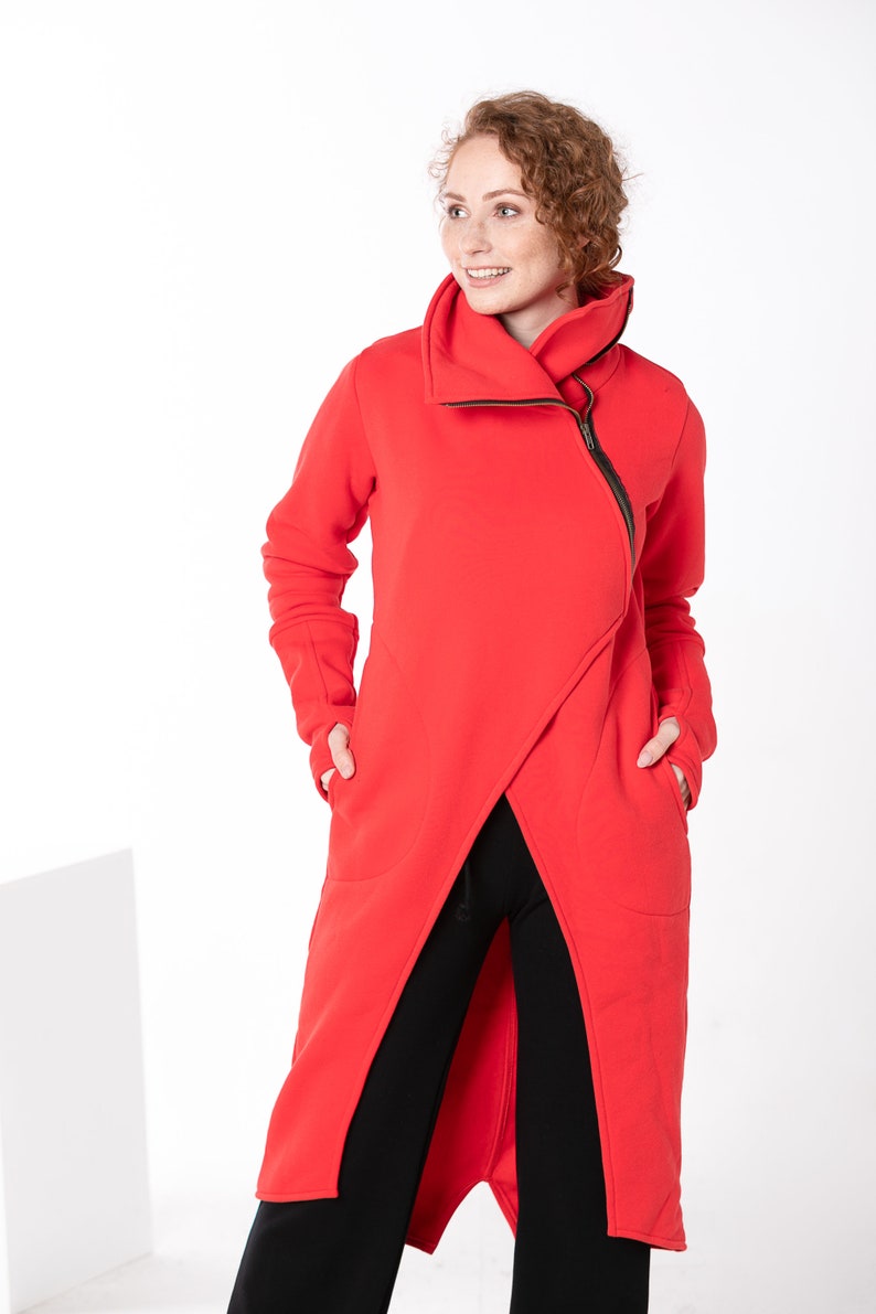 May include: A long red hooded sweatshirt with a zipper and pockets. The sweatshirt has a long, asymmetrical hemline.