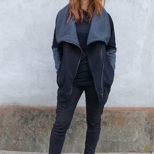 Pu&ograve; includere: Una donna indossa una giacca nera e grigia con cerniera e un colletto grande, pantaloni neri e stivaletti neri.