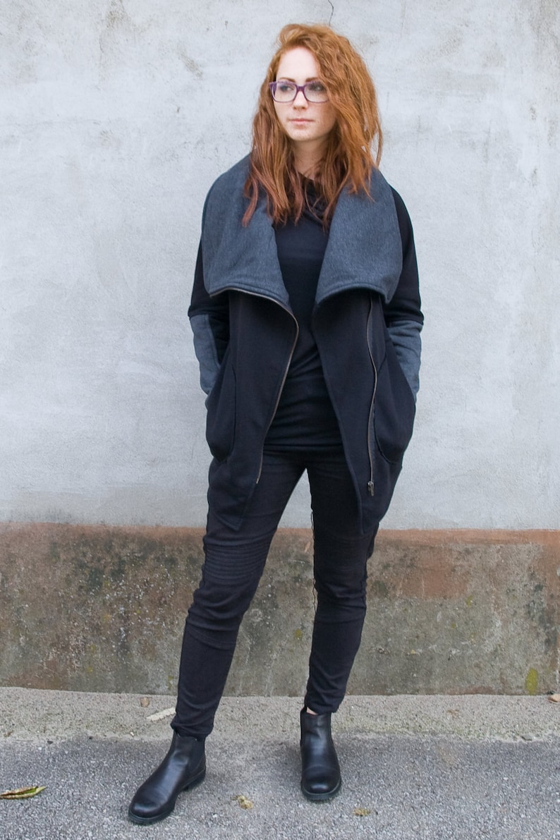 Pu&ograve; includere: Una donna indossa una giacca nera e grigia con cerniera e un colletto grande, pantaloni neri e stivaletti neri.