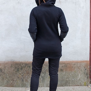 Pu&ograve; includere: Una tunica nera a maniche lunghe con un collo alto e una vestibilit&agrave; rilassata. La tunica &egrave; indossata con pantaloni neri e stivaletti neri.