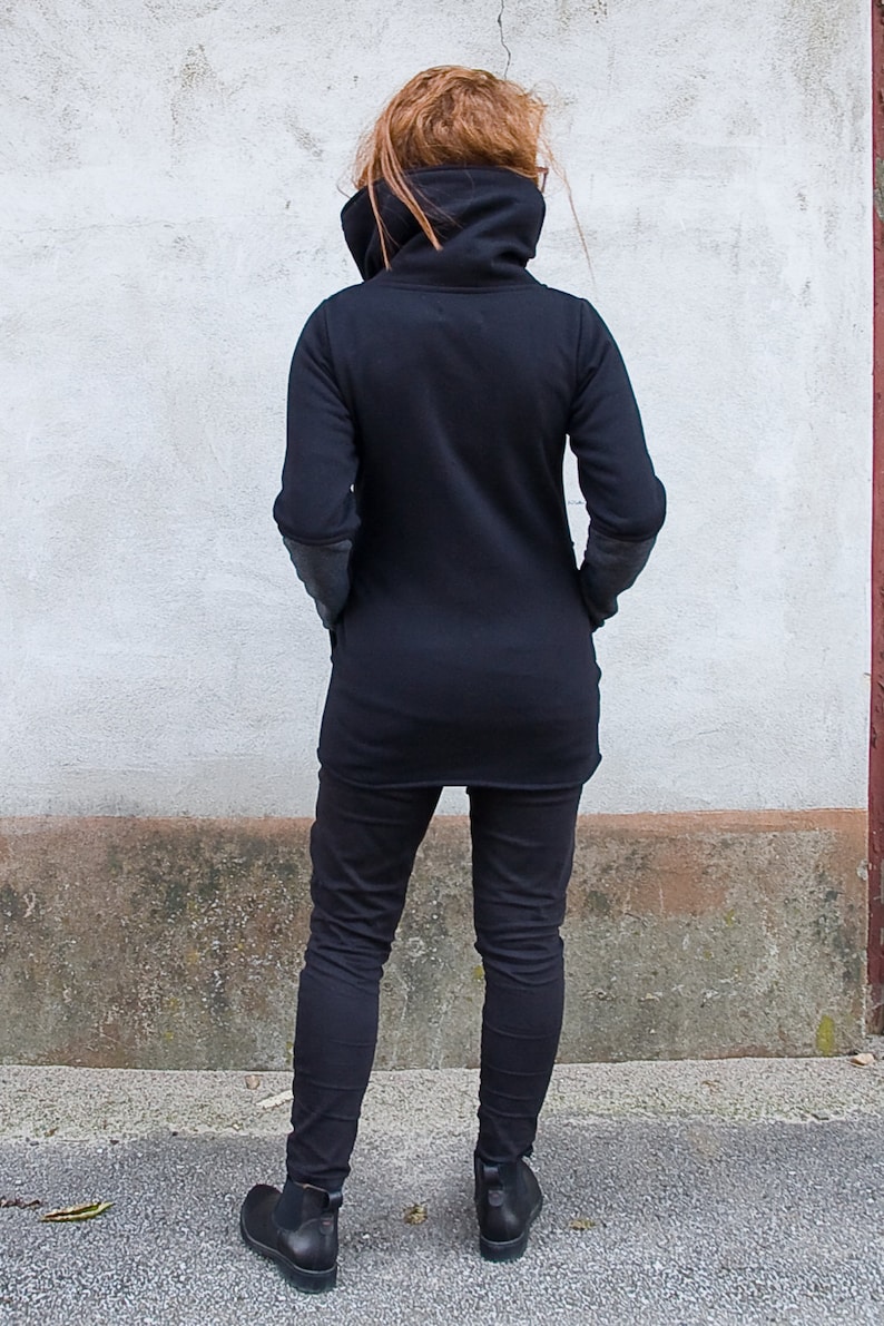 Pu&ograve; includere: Una tunica nera a maniche lunghe con un collo alto e una vestibilit&agrave; rilassata. La tunica &egrave; indossata con pantaloni neri e stivaletti neri.
