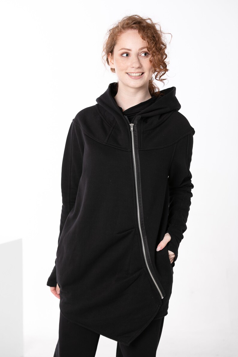 May include: A black hooded sweatshirt with a long zipper down the front and a slightly asymmetrical hem. The sweatshirt has a relaxed fit and a casual style.