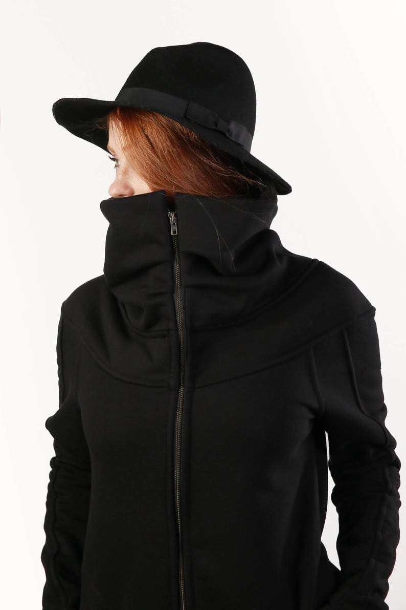 May include: A black zip-up jacket with a high, folded collar and long sleeves. The jacket has a zipper closure and a black fedora hat is worn on top of the head.