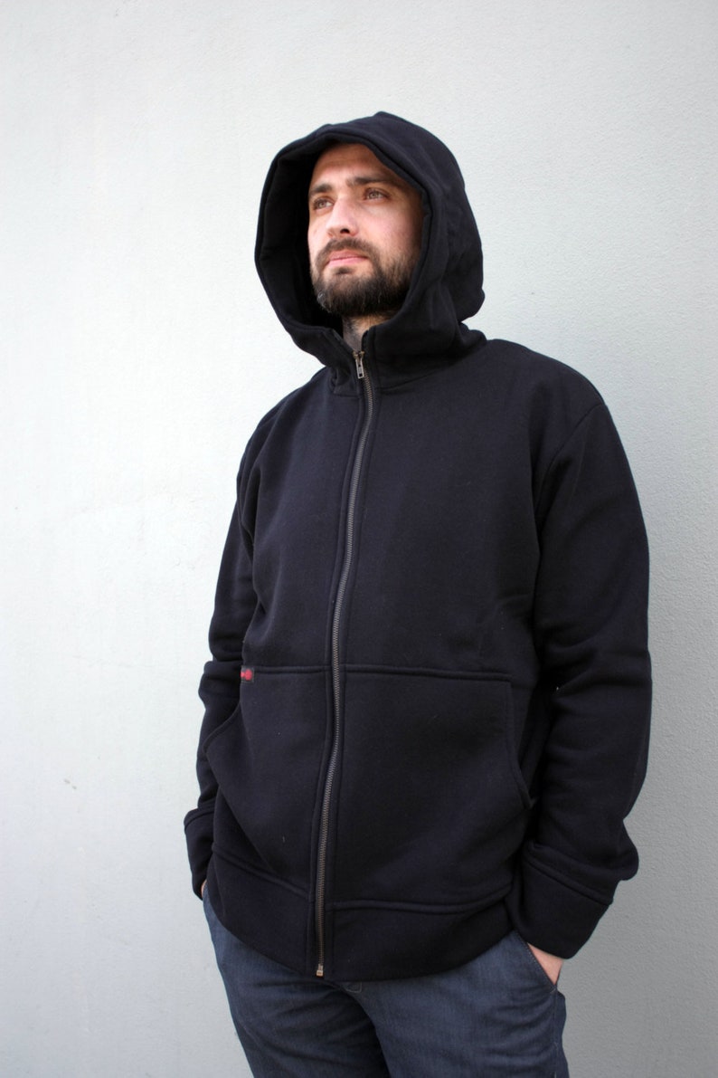 Pu&ograve; includere: Una felpa con cappuccio nera con zip. La felpa ha una chiusura a zip e una tasca sul davanti. La persona indossa jeans blu.
