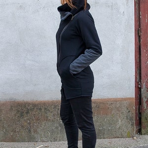 Pu&ograve; includere: Una giacca nera a maniche lunghe con cerniera e colletto alto. La giacca ha un pannello grigio sulla manica. La persona indossa pantaloni neri e stivaletti neri.