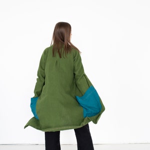 May include: A long green linen jacket with teal blue fabric panels on the sides. The jacket is worn by a person with long brown hair, but the person's face is not visible.