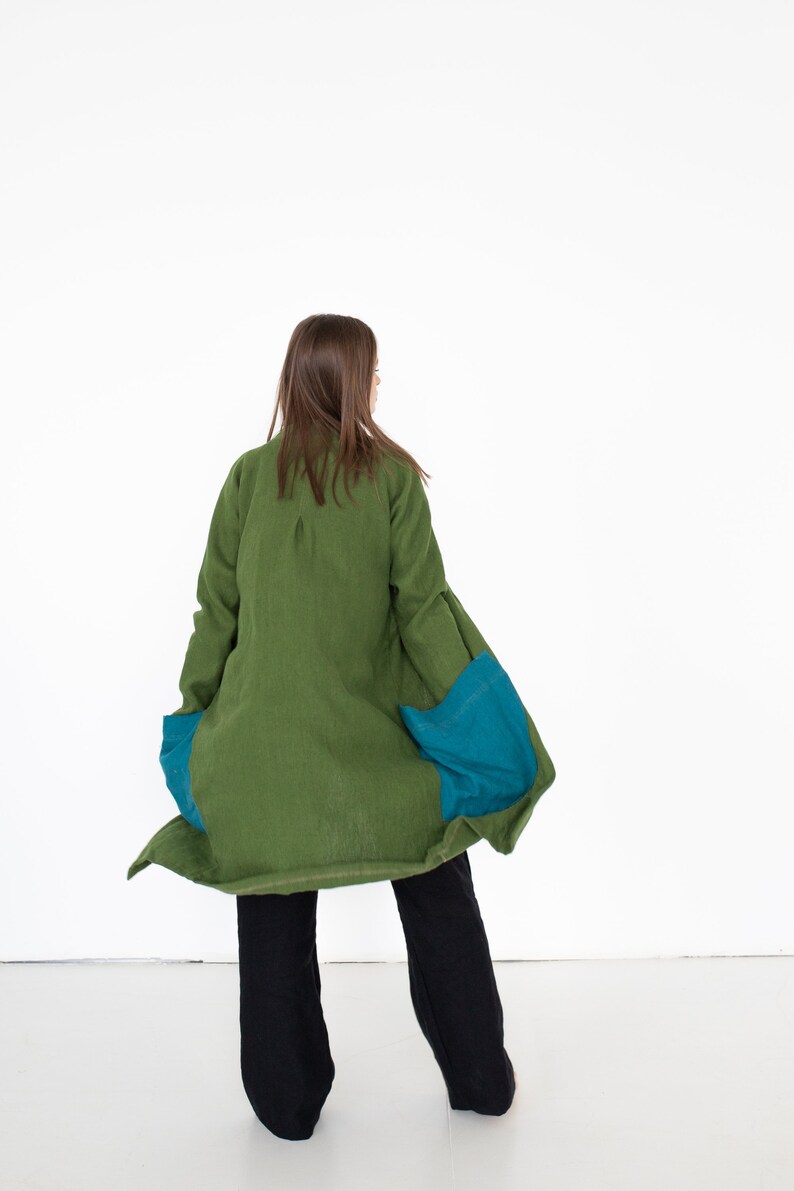 May include: A long green linen jacket with teal blue fabric panels on the sides. The jacket is worn by a person with long brown hair, but the person's face is not visible.