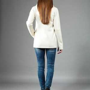May include: A woman wearing a white long-sleeved shirt and blue jeans. She is standing with her back to the camera.