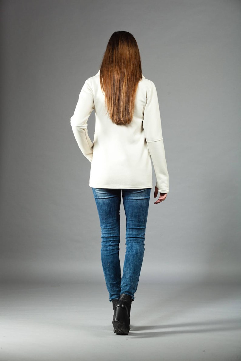 May include: A woman wearing a white long-sleeved shirt and blue jeans. She is standing with her back to the camera.