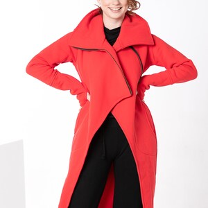 May include: A long red hooded jacket with a zipper closure and a draped design. The jacket has two pockets on the sides.