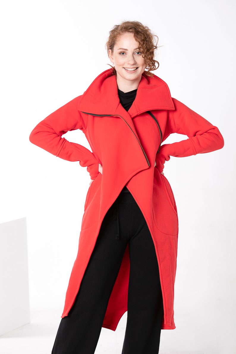 May include: A long red hooded jacket with a zipper closure and a draped design. The jacket has two pockets on the sides.