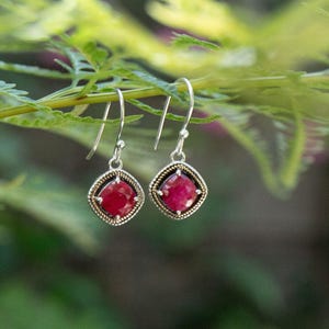 Puede incluir: Un par de pendientes de plata con una piedra preciosa roja en un engaste cuadrado. Los pendientes tienen un diseño delicado y son perfectos para el uso diario.