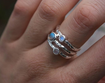 Könnte beinhalten: Ein silberner Ring mit drei Mondstein-Edelsteinen, die in einem strukturierten Band gefasst sind. Der Ring wird an einem Finger getragen.