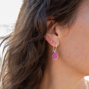 Peut inclure: Boucles d'oreilles en argent avec des pierres roses. L'une est un petit clou carré, l'autre en forme de goutte. Les pierres ont une bordure argentée. Les boucles d'oreilles sont mises en valeur sur un fond flou.