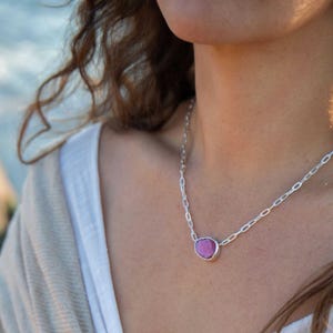 May include: A silver chain necklace featuring a large, irregularly shaped, pink gemstone pendant. The pendant is set in a silver bezel. The necklace is worn around the neck.