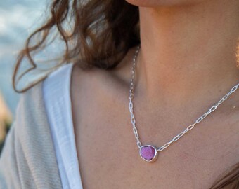 May include: A silver chain necklace with a large, irregular-shaped, pink gemstone pendant. The pendant is set in a silver bezel. The necklace is worn around the neck.