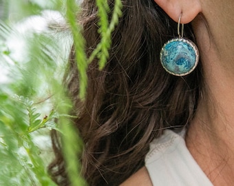 May include: A pair of silver earrings with a round blue and green stone set in a silver bezel.